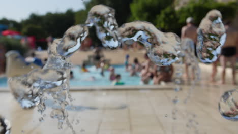 Water-fountain-in-slow-motion-in-a-camping,-people-chilling-in-a-pool-background